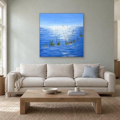 Blue square water painting in a silver-tone frame above a cream sofa against a pale grey-green wall