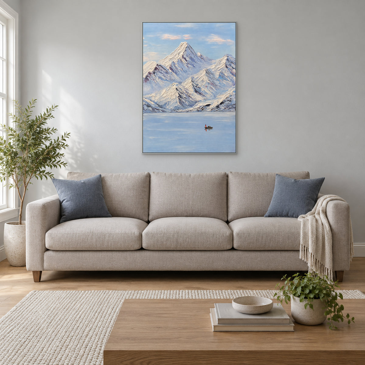 Vertical snowy mountain painting in a silver-tone floating frame centred above a neutral living-room sofa