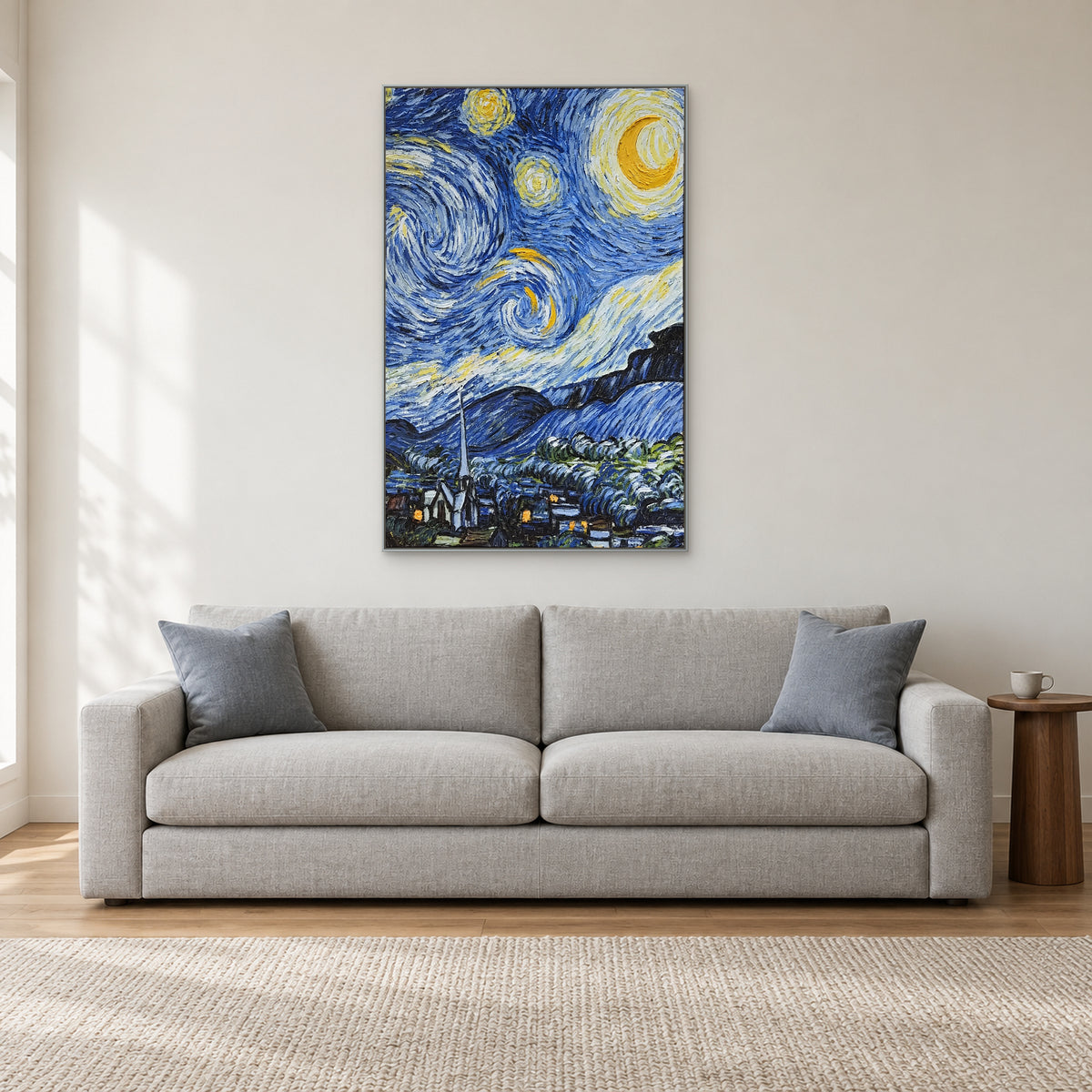 Vertical moonlit village artwork in a silver-tone frame, centred above a grey living-room sofa.