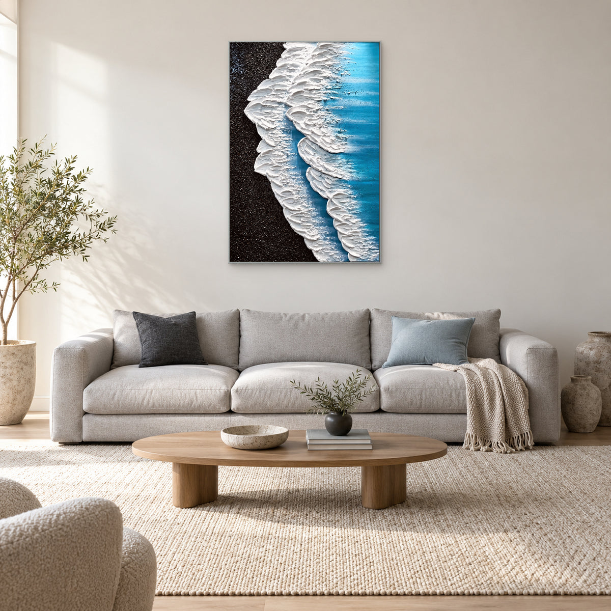 Coastal wave painting in a silver-tone frame centred over a pale sofa with blue and charcoal cushions