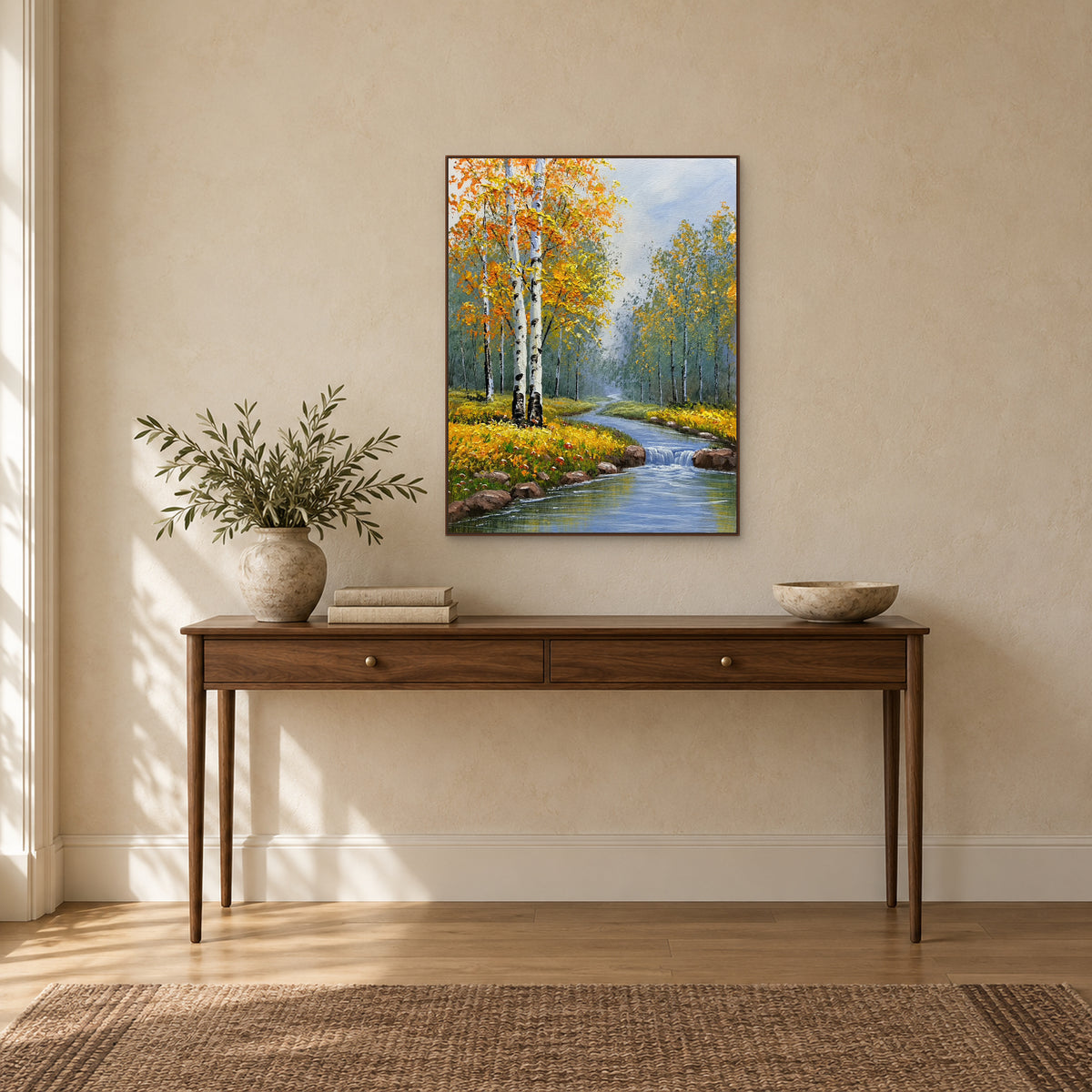 Birch woodland and blue stream painting in a walnut-tone frame above a console, clear of leafy branches on the left.