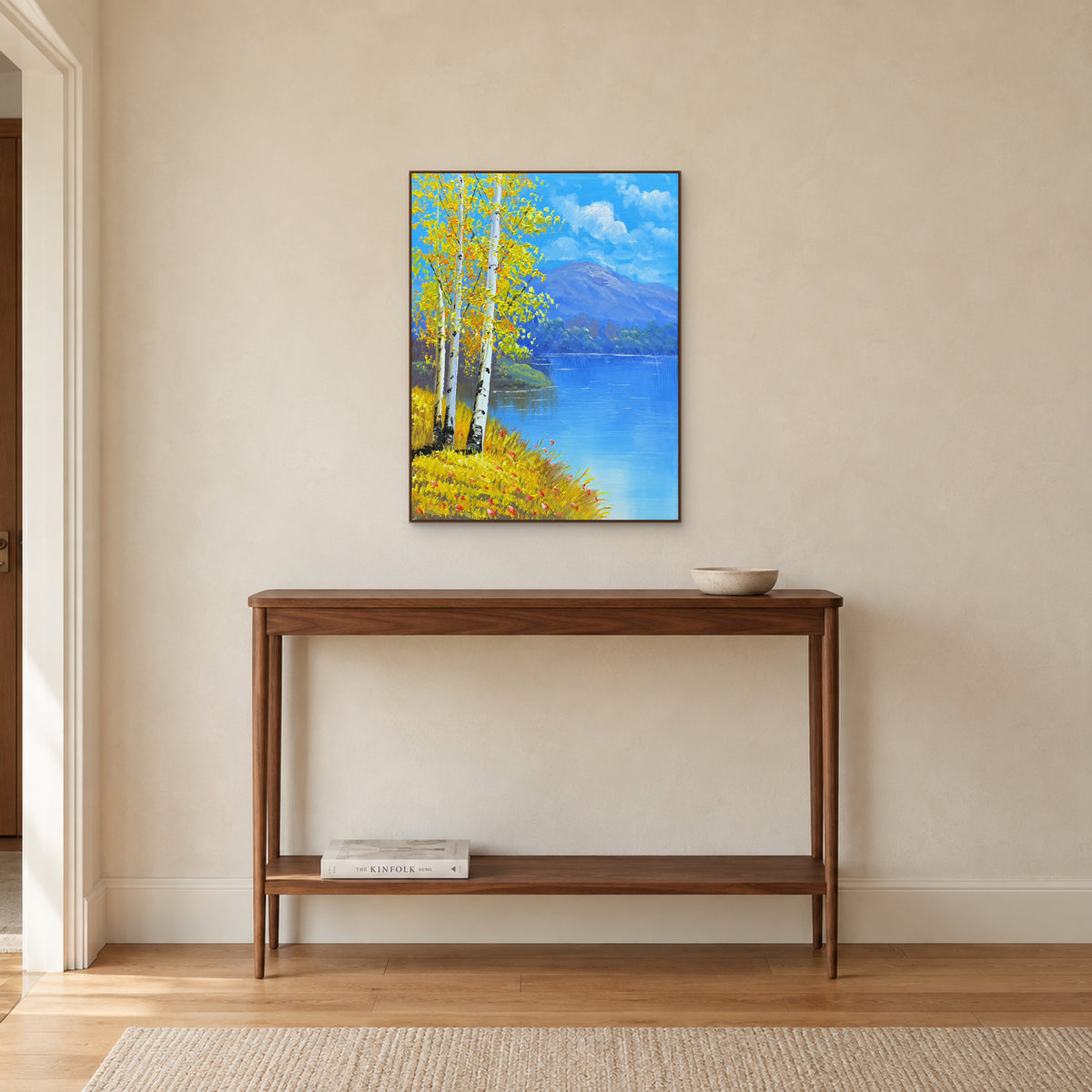 Birch lakeshore painting in a walnut-toned frame above a narrow wooden console on a warm wall.