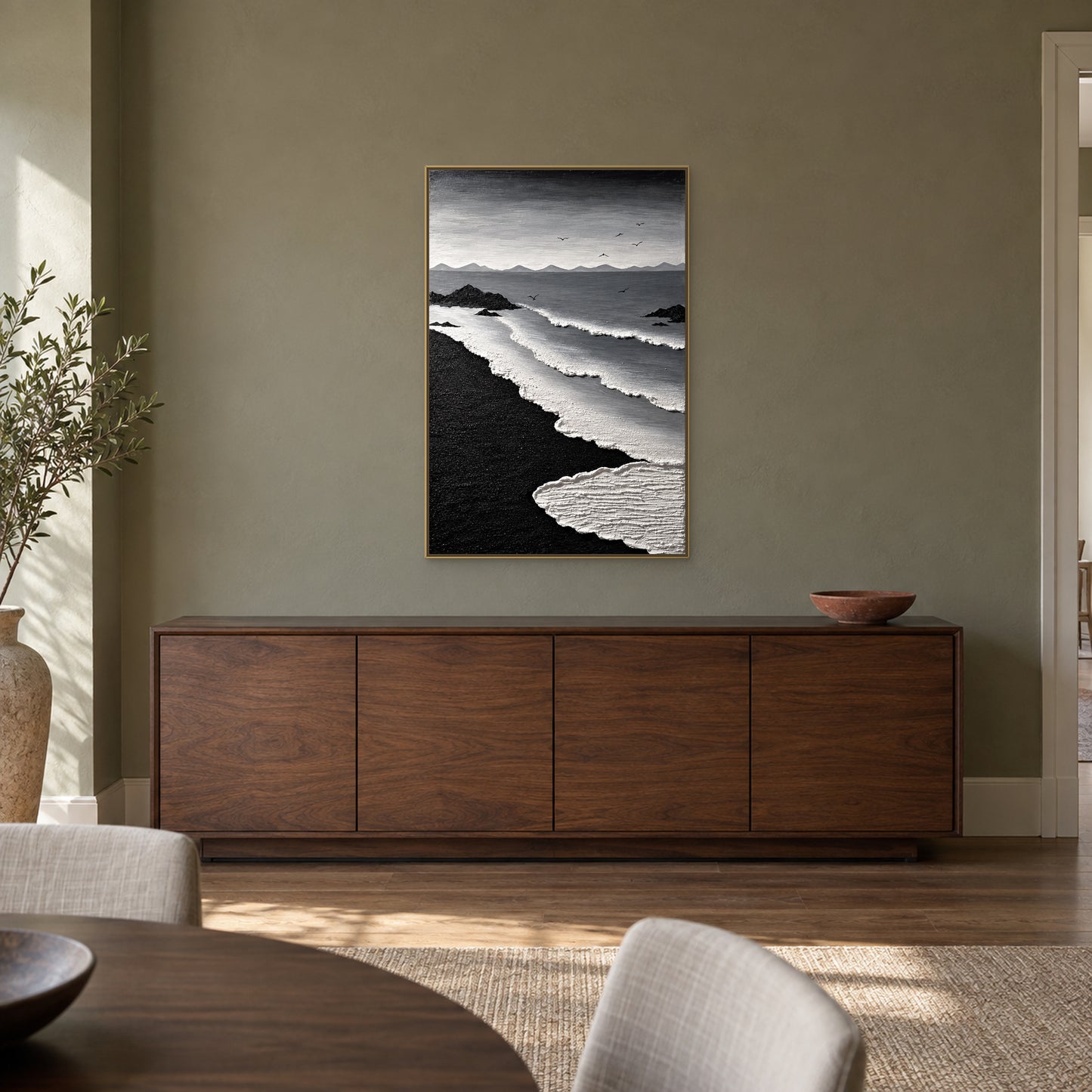 Vertical black and white seascape in a champagne-tone floating frame above a walnut-tone sideboard against an olive-grey dining-room wall
