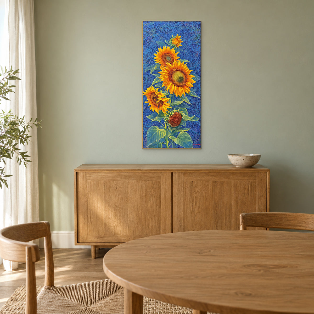 Champagne-framed sunflower painting above a wooden sideboard against a muted green dining-room wall