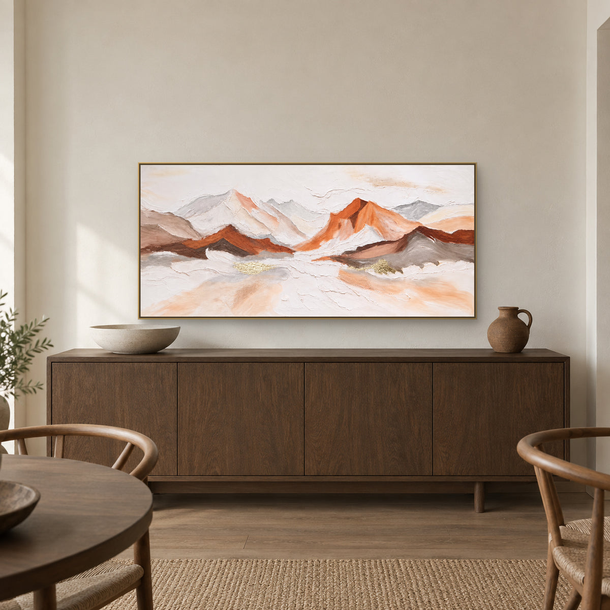 Ivory and copper mountain painting in a champagne-tone floating frame above a dark credenza with low ceramics