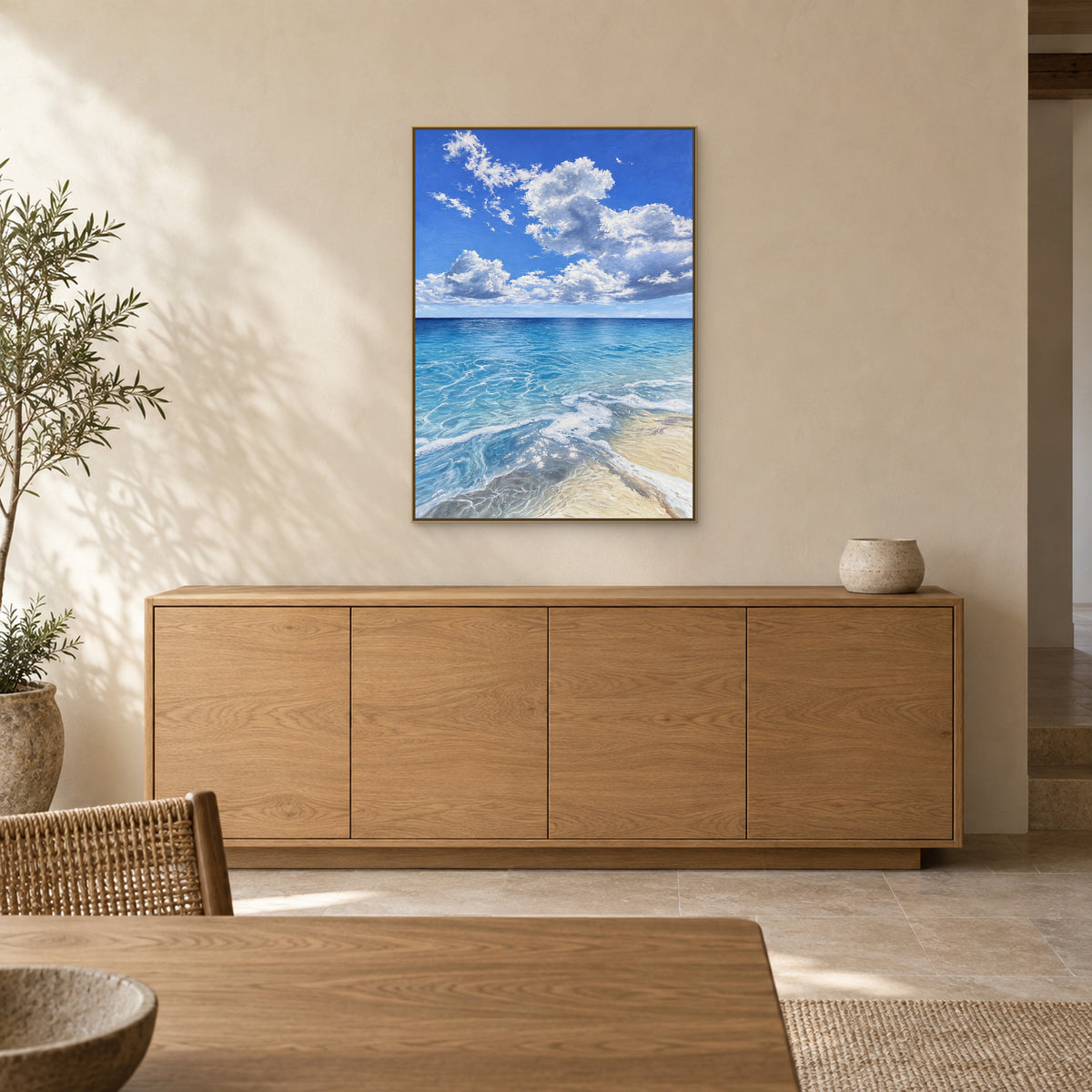 Blue coastal painting in a champagne-tone floating frame above an oak sideboard in a dining area