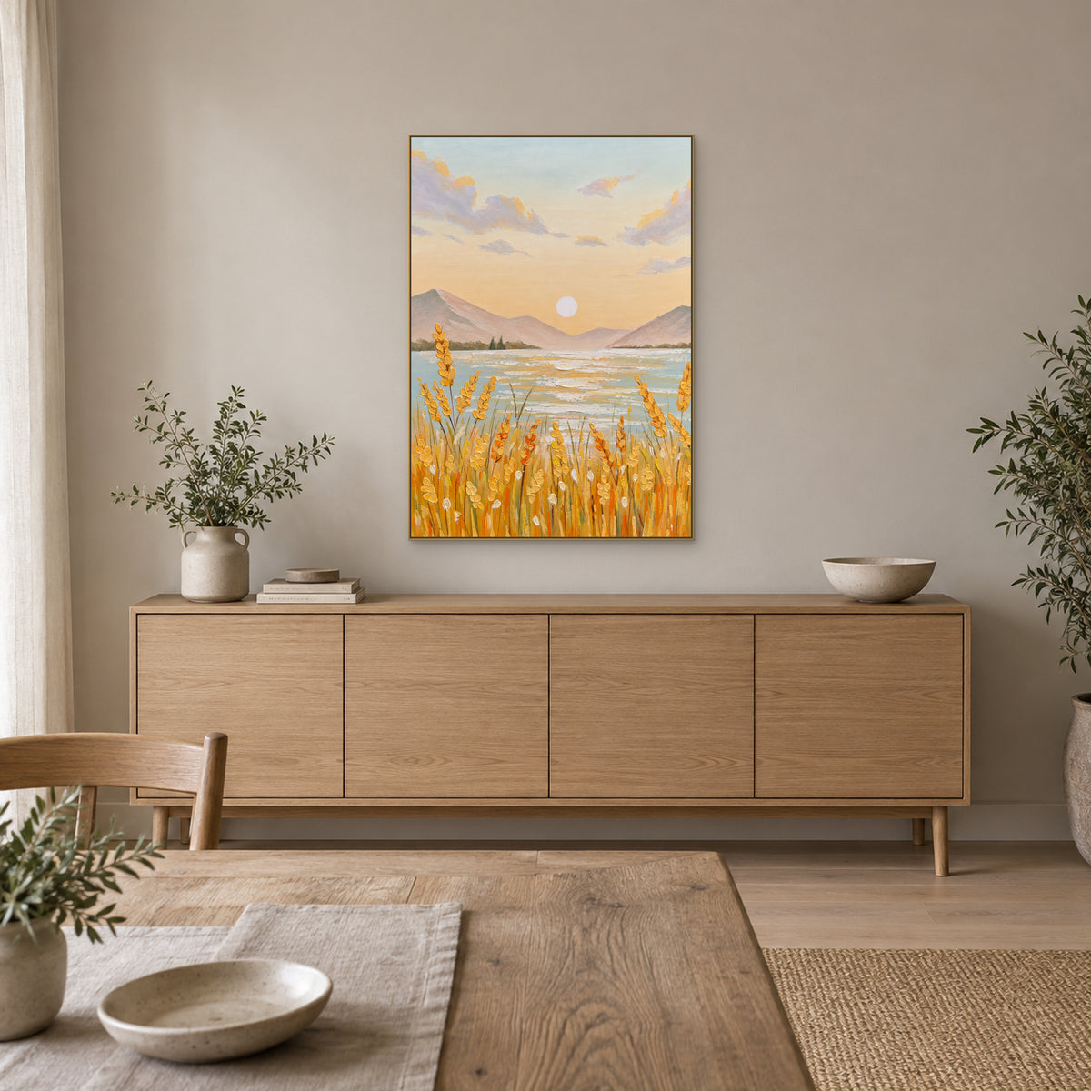 Pastel lake and golden grain painting in a champagne-tone frame centred above an oak-tone sideboard