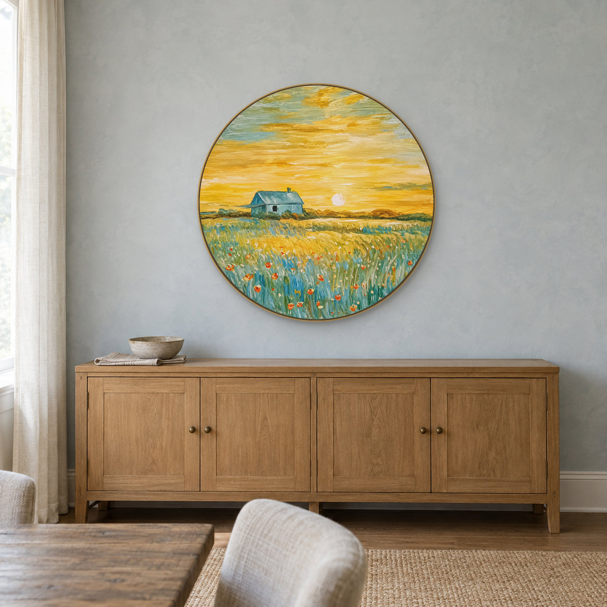 Round cottage landscape in a champagne-tone frame above a wooden cabinet against a blue-grey wall