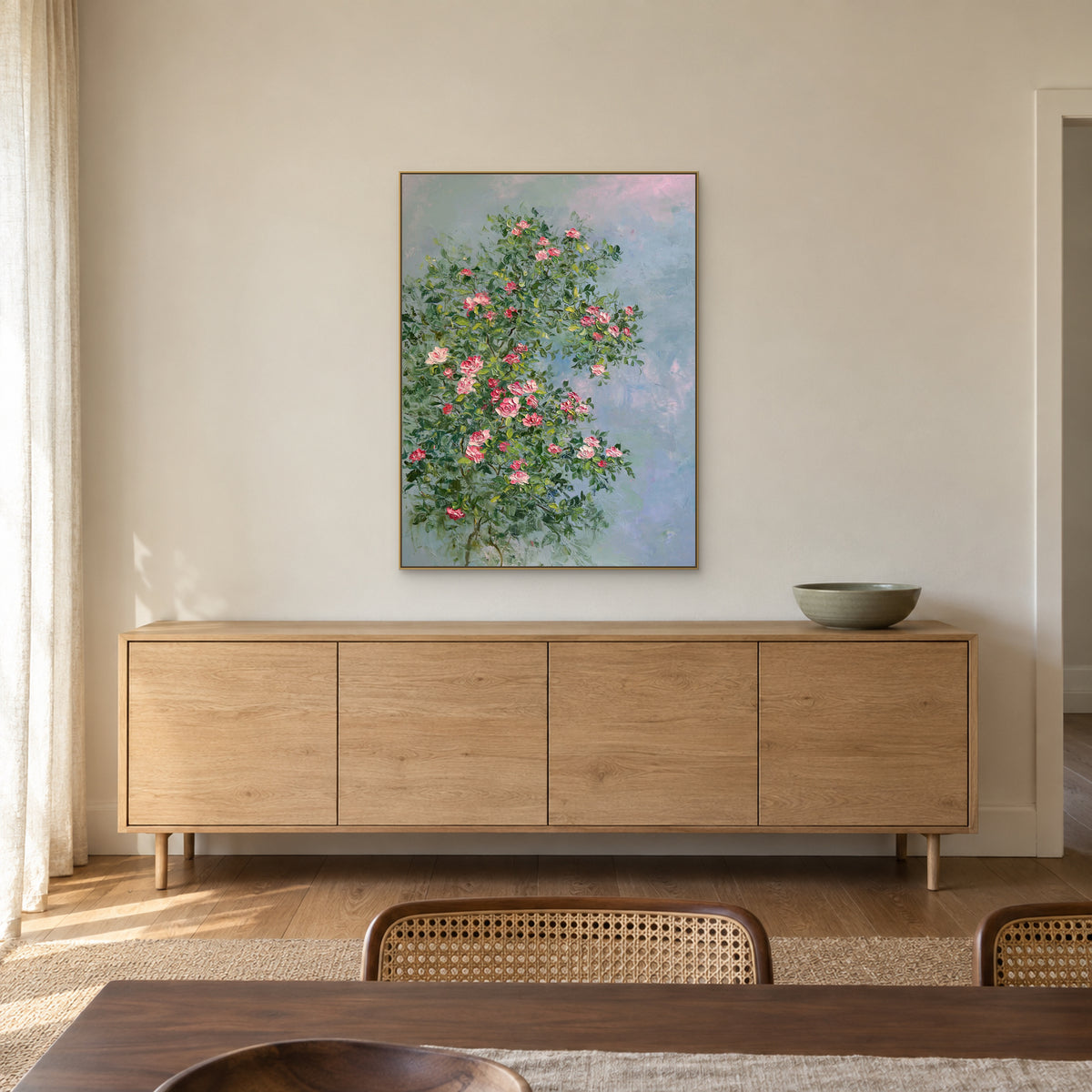 Pink rose painting in a thin champagne-tone floating frame above a wooden sideboard in a dining area