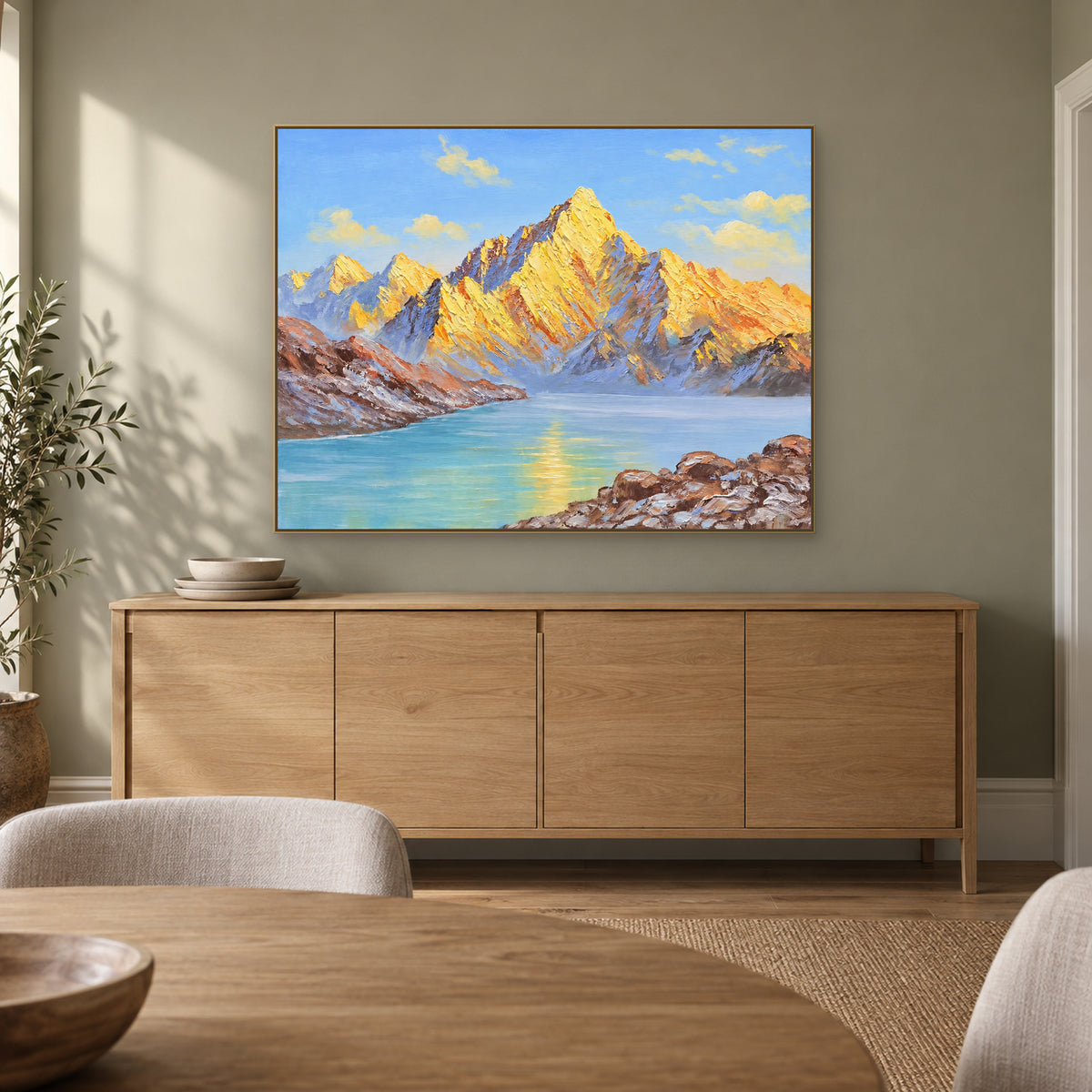 Golden mountain lake painting in a champagne-tone frame above a pale wood dining-room sideboard