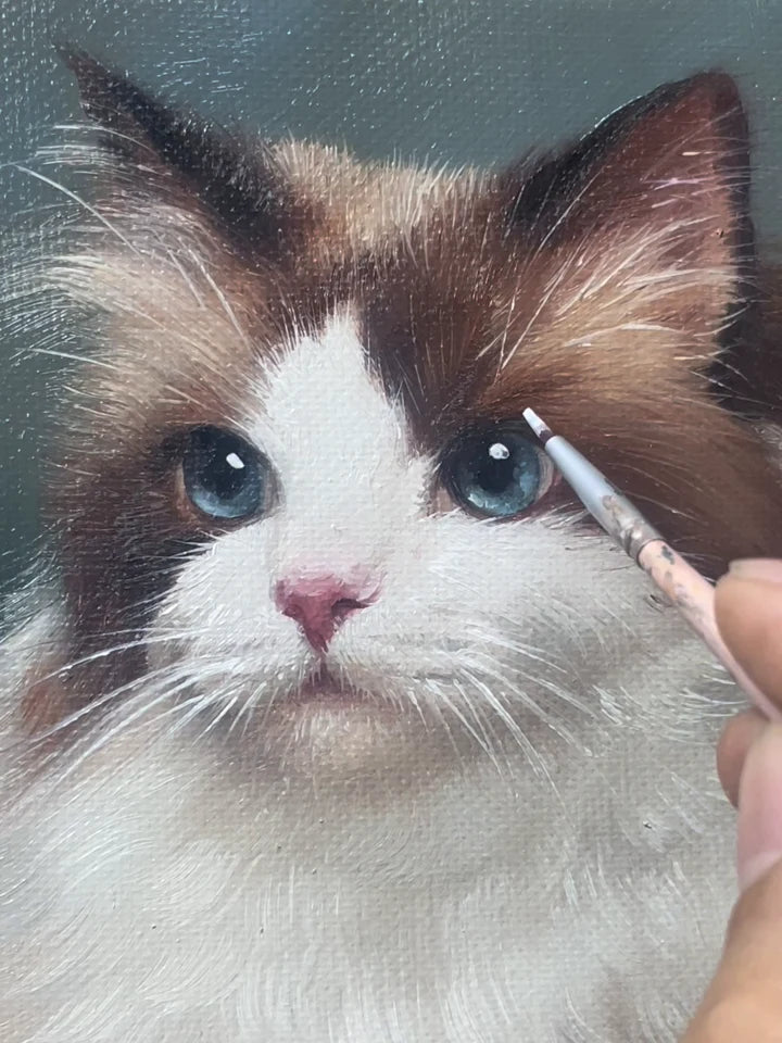 A brush adding fine detail around the blue eye of a hand-painted cat portrait