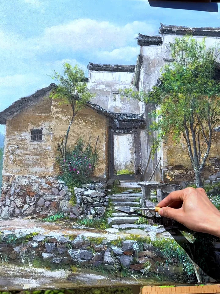 A palette knife adding detail to a painting of traditional village houses and a stone path