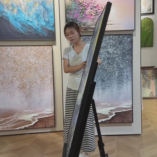 A person turns the blue and yellow starry village painting from its edge towards a full front view in a gallery.