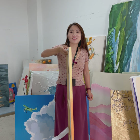 A person turns a narrow orange sailboat painting to show its front, followed by a framed wall display