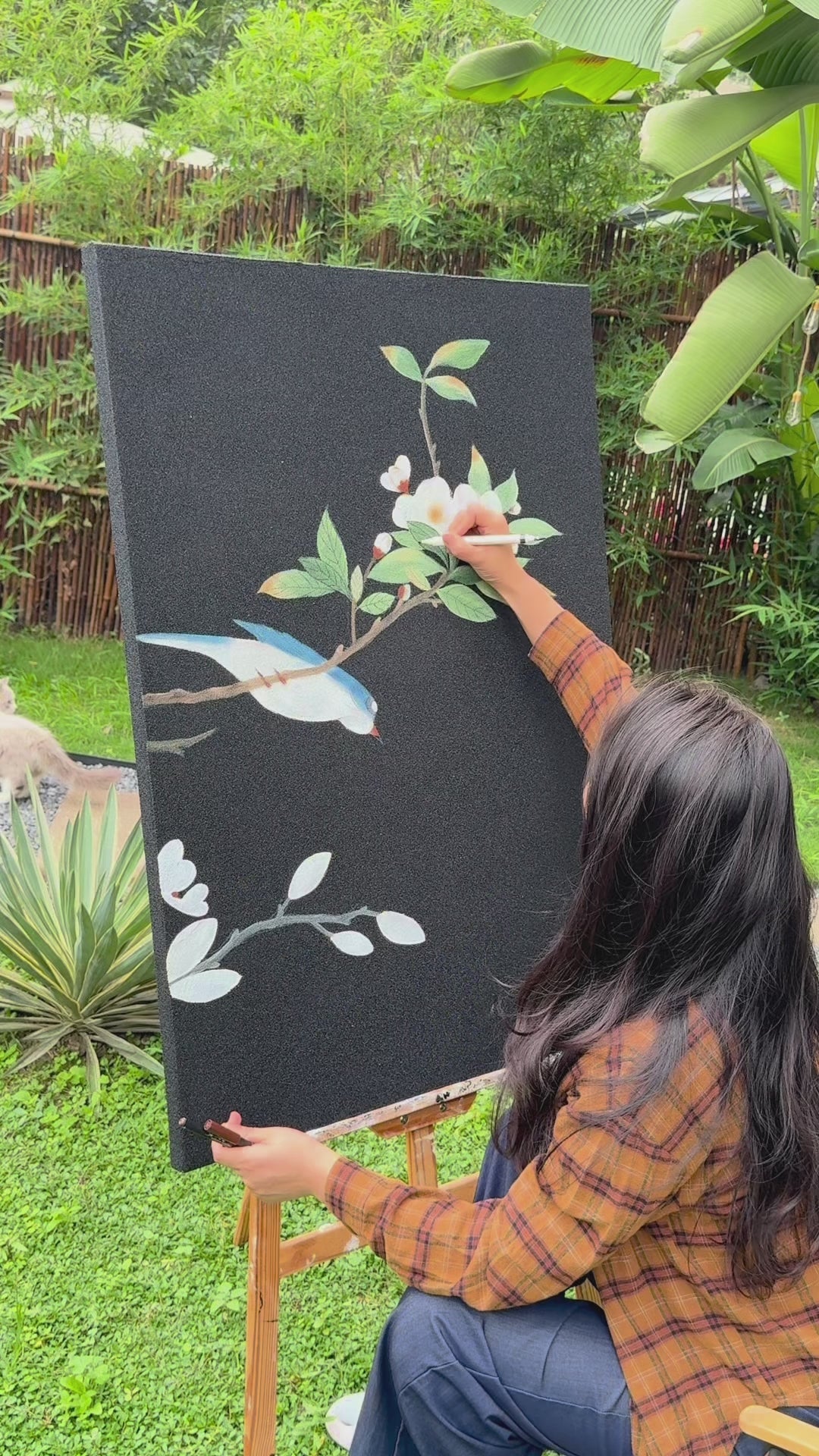 Two painting-process views of a blue bird and flowering branches on a dark canvas