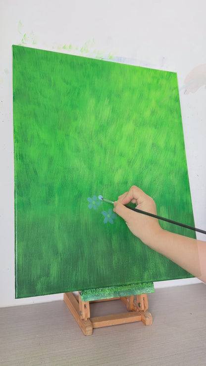 A hand paints small blue flax flowers across a green canvas, followed by the completed floral painting